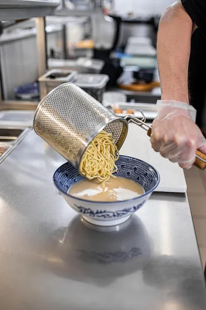 Chef versant des nouilles fraîches égouttées dans un bol en cuisine